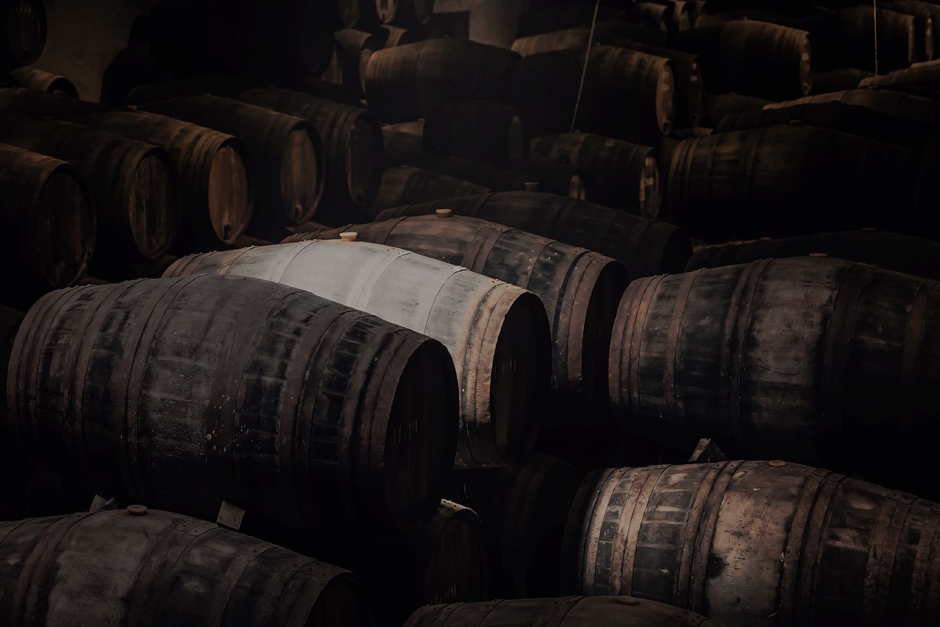 Rows of maturing oak whisky casks in a dimly lit warehouse